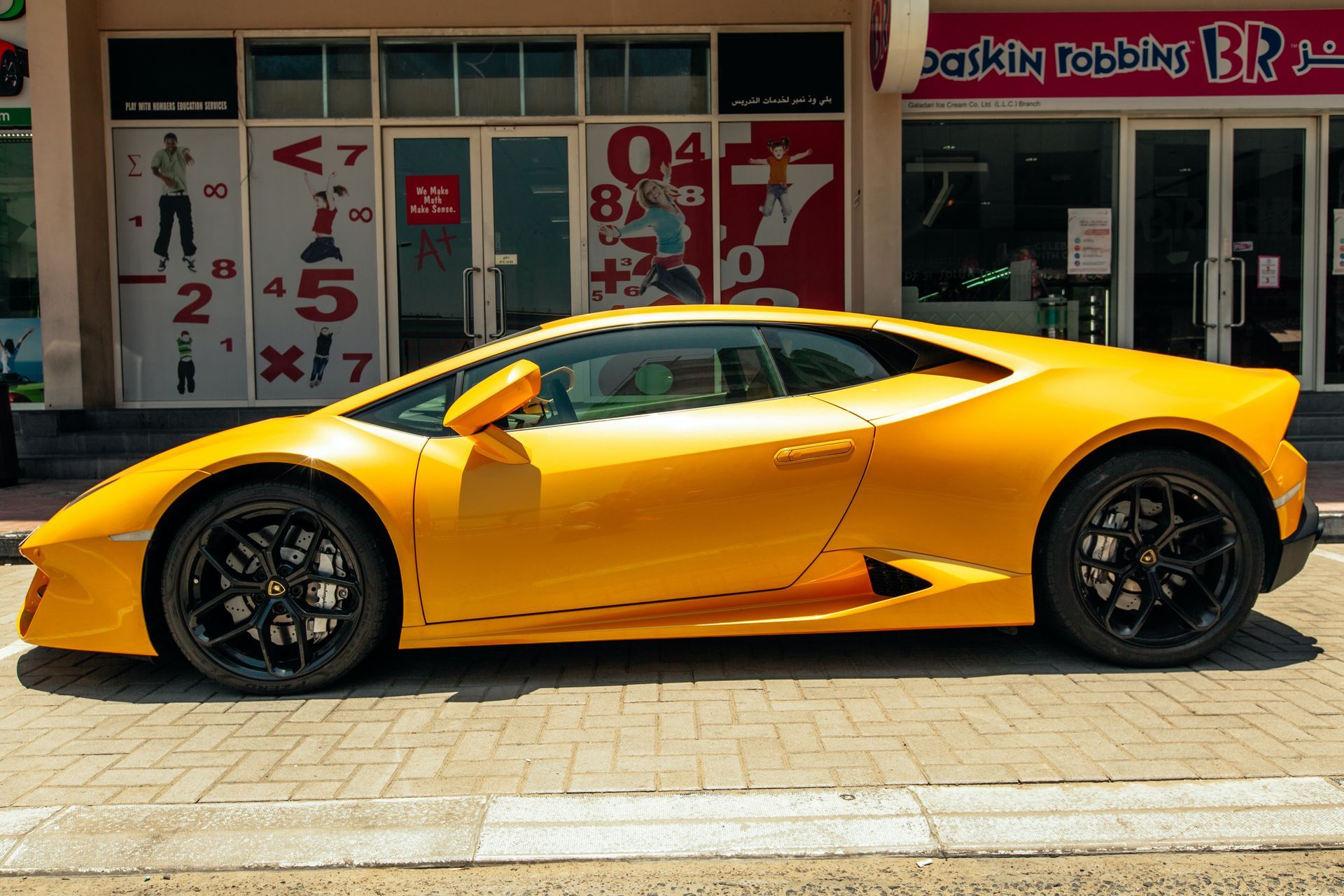A yellow sports car is parked in front of a building that says bakkin robbins