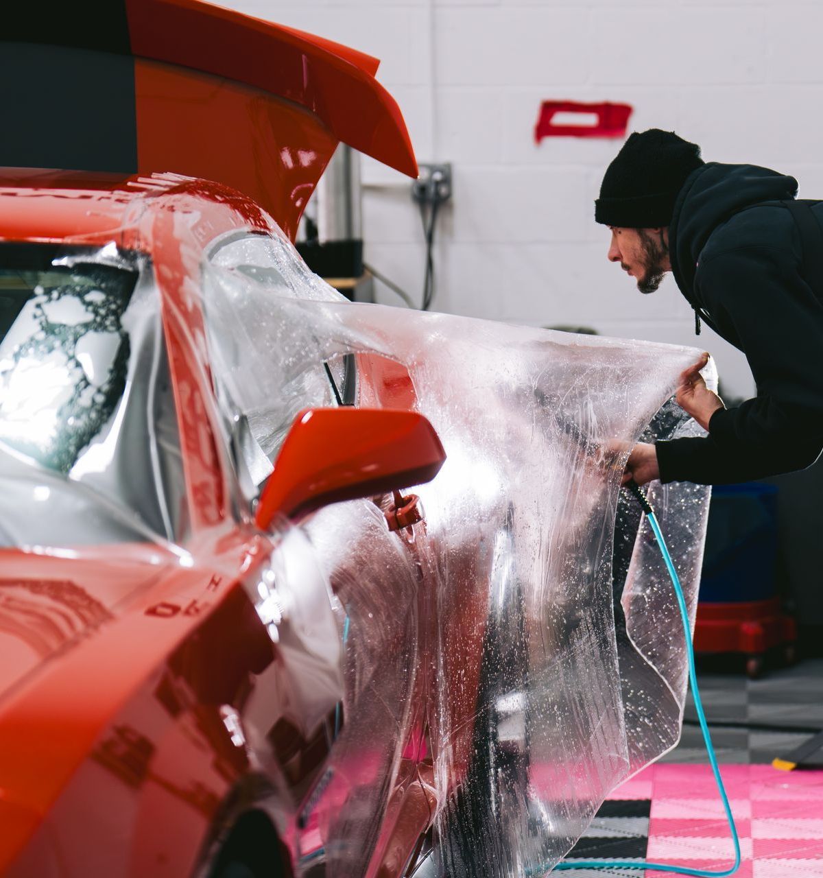 A man is wrapping a red car in plastic