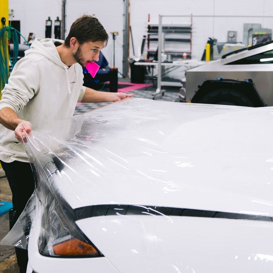 A person wearing black gloves is polishing the hood of a red car.