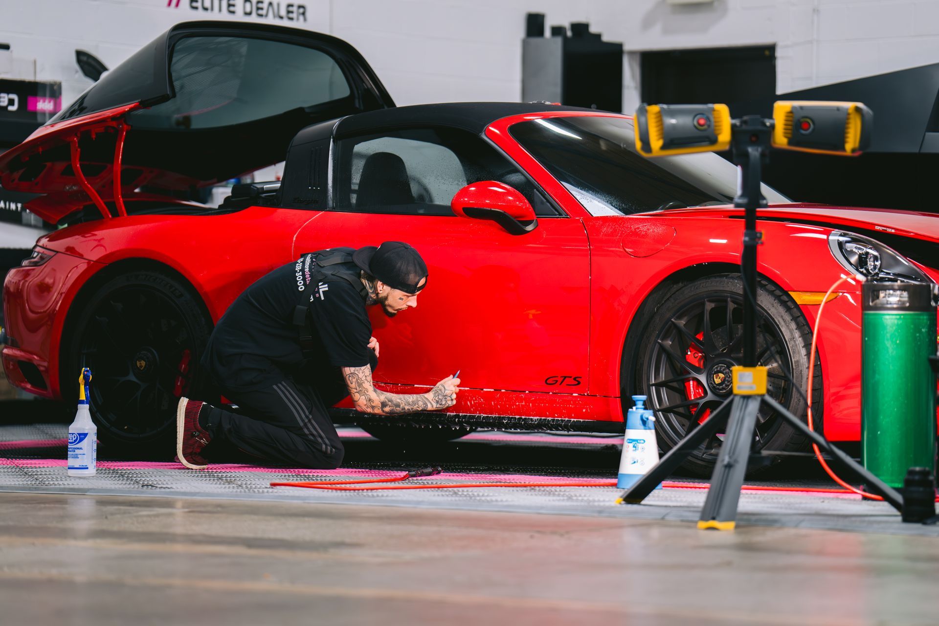 A man is polishing a black car with a sponge and a spray bottle.
