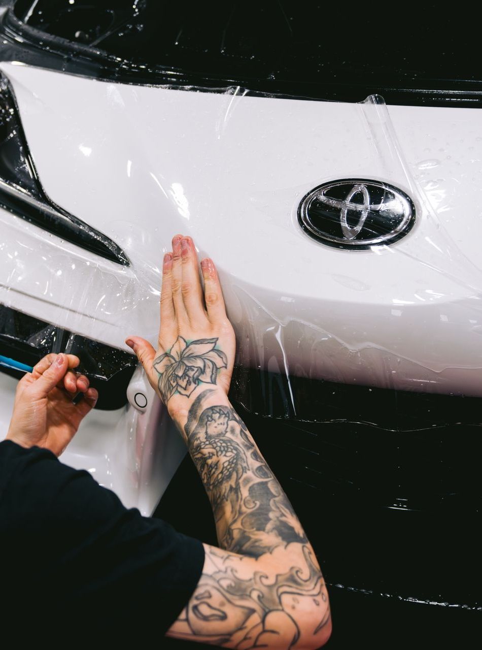 A person wearing black gloves is polishing a black car