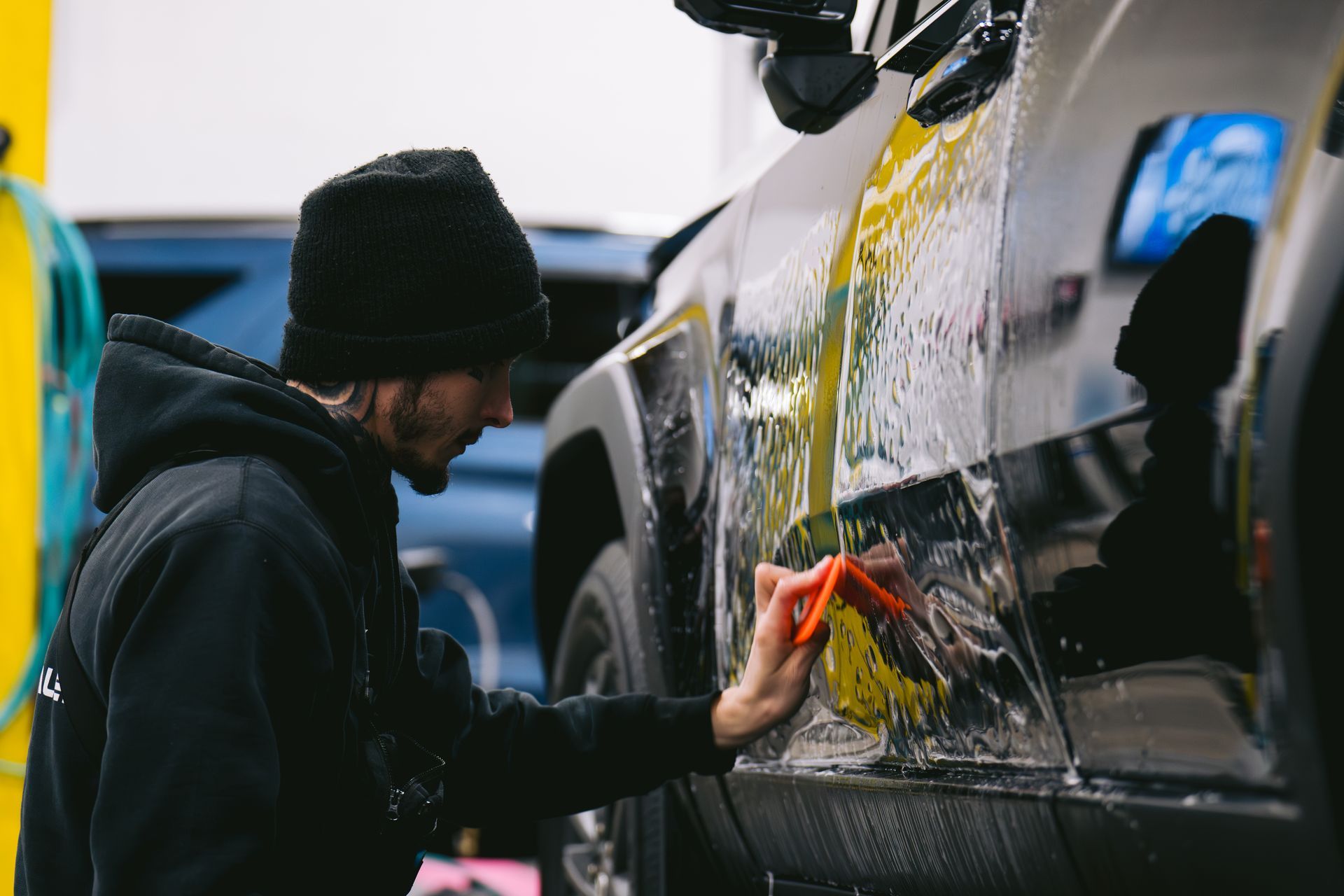 A person is holding a blue sponge in front of a car.