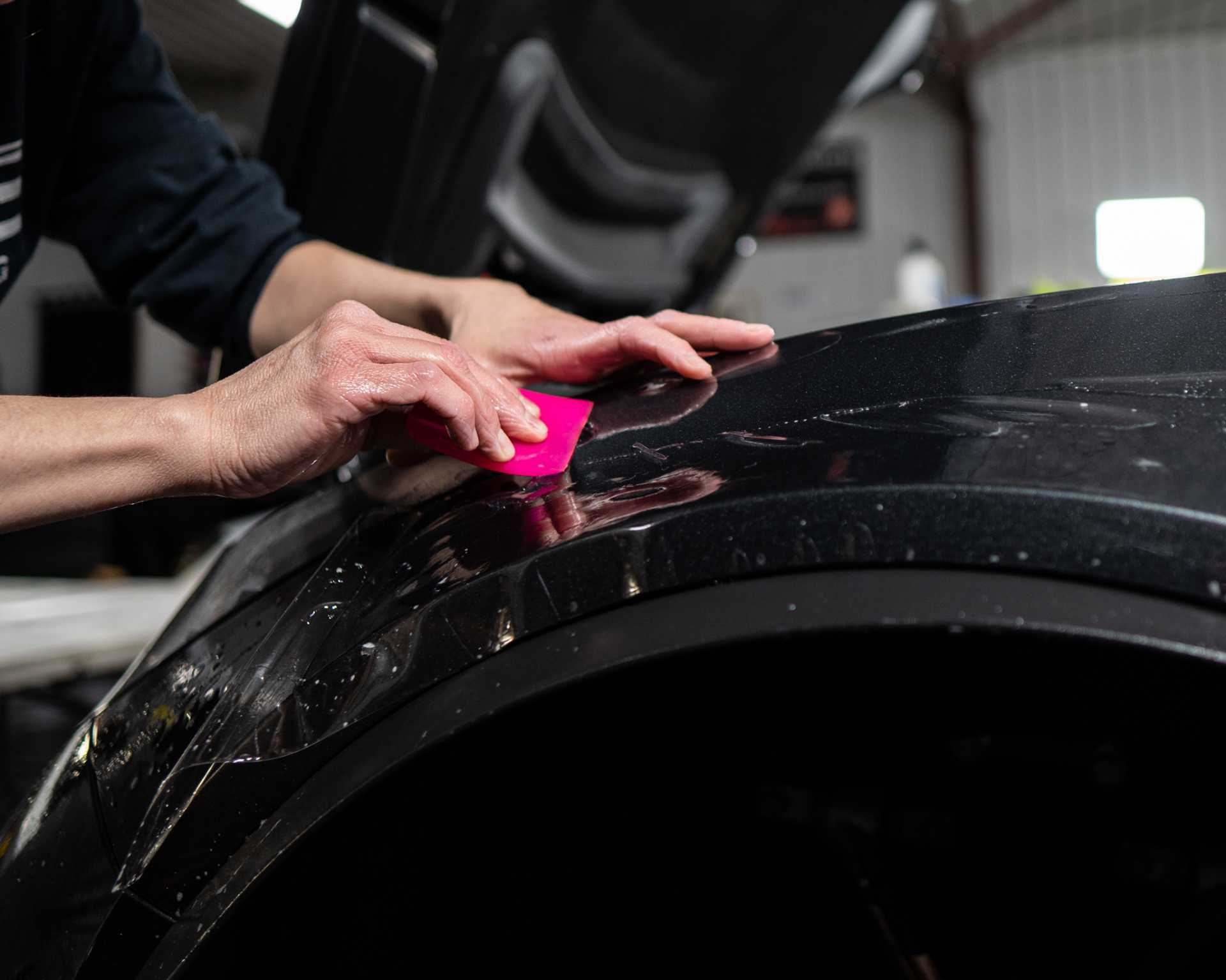 A person is applying a protective film to the fender of a car.