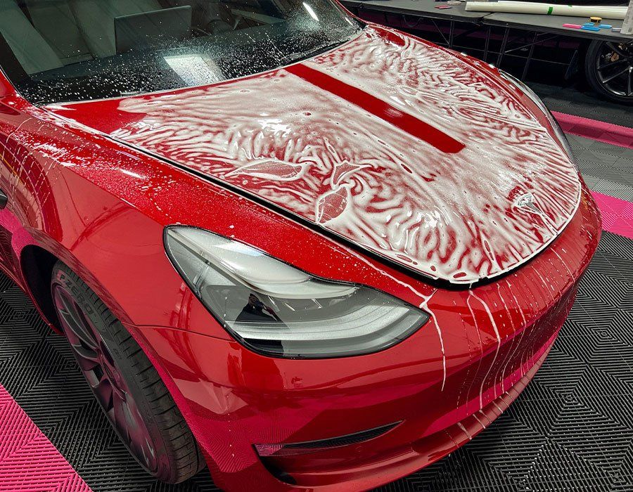 The hood of a red tesla model 3 is covered in foam.