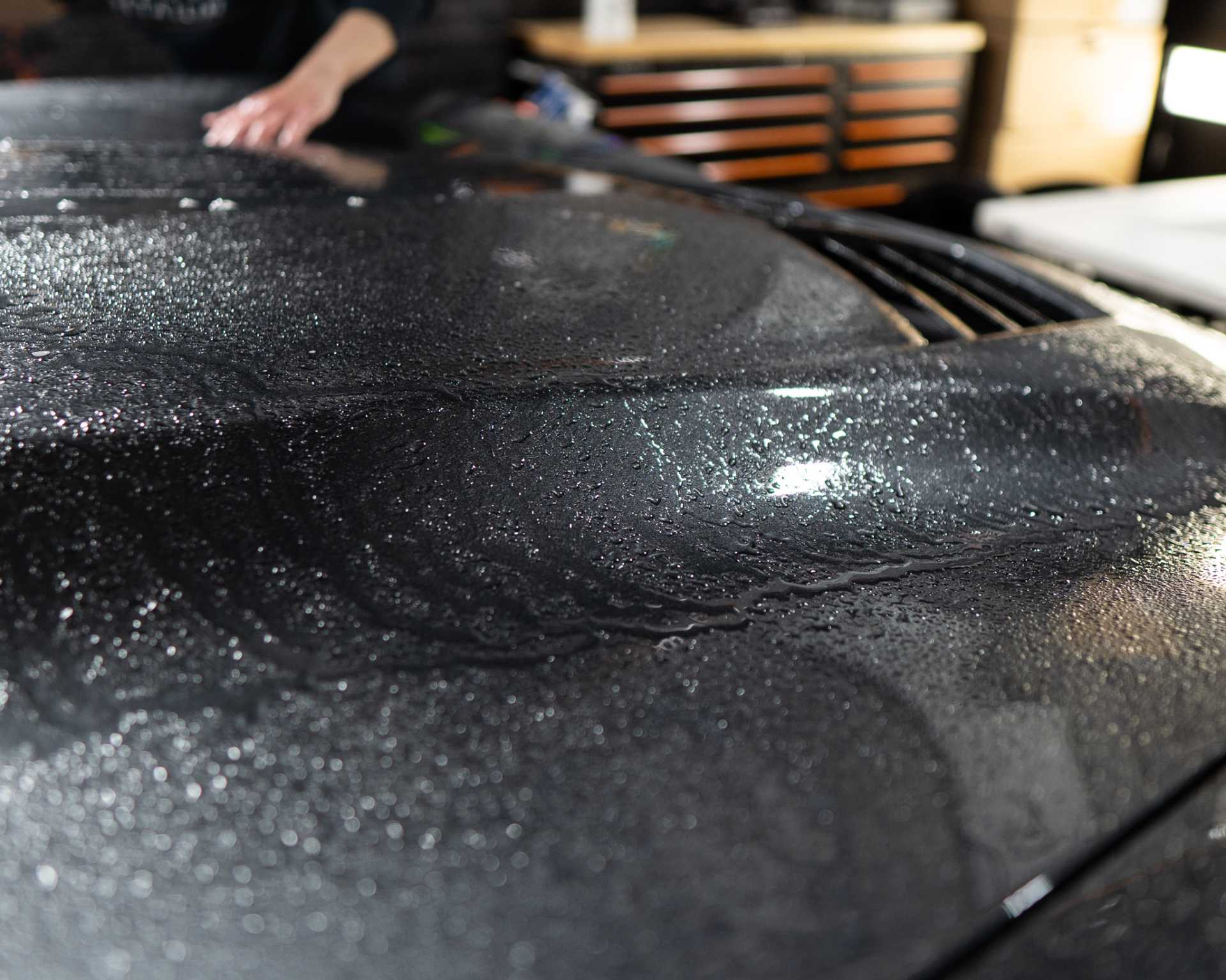 A person is cleaning the hood of a black car