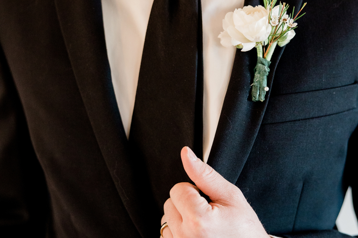 A man in a tuxedo is holding a white rose in his pocket.