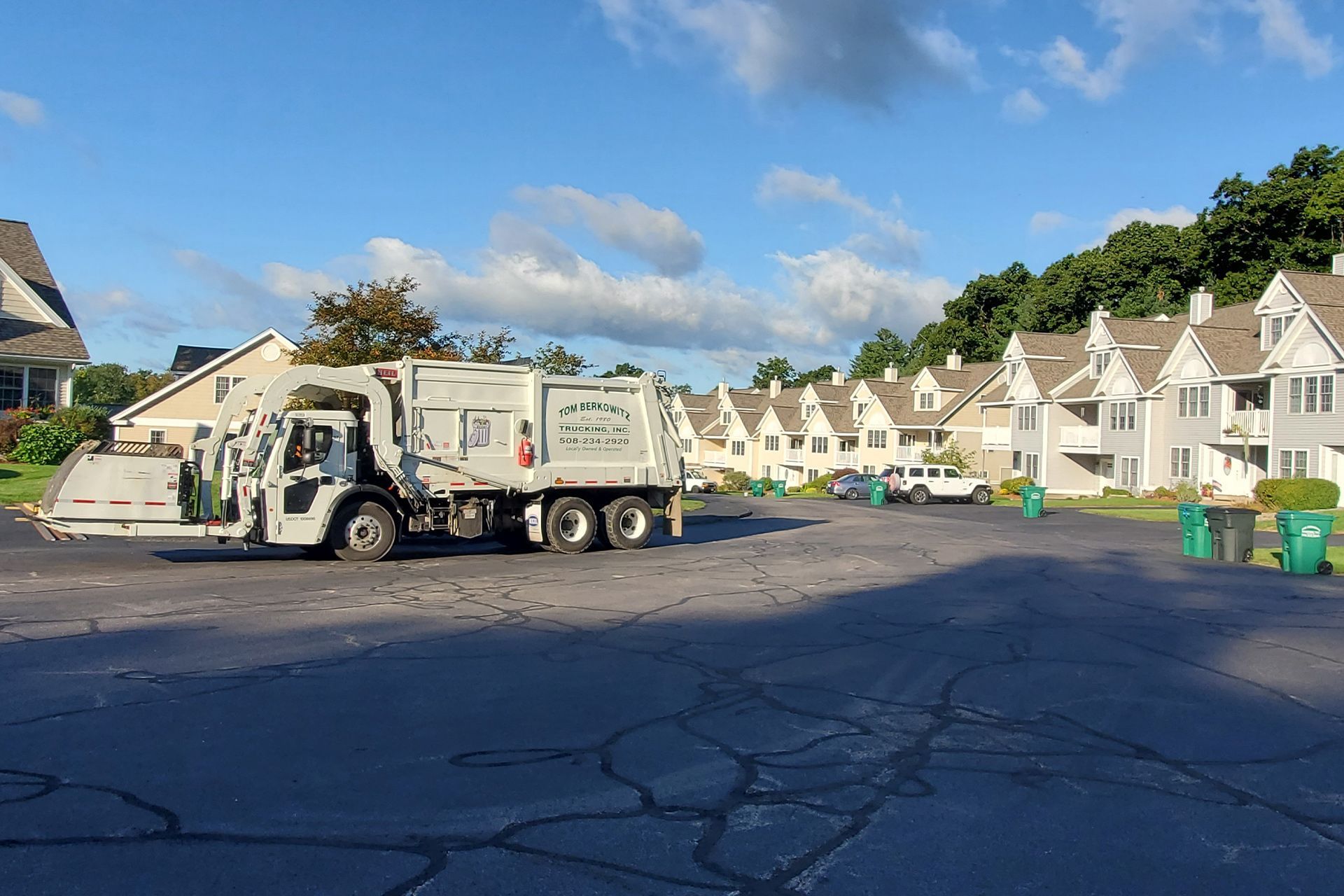 Garbage truck collecting trash in a residential area with townhouses under a blue sky.