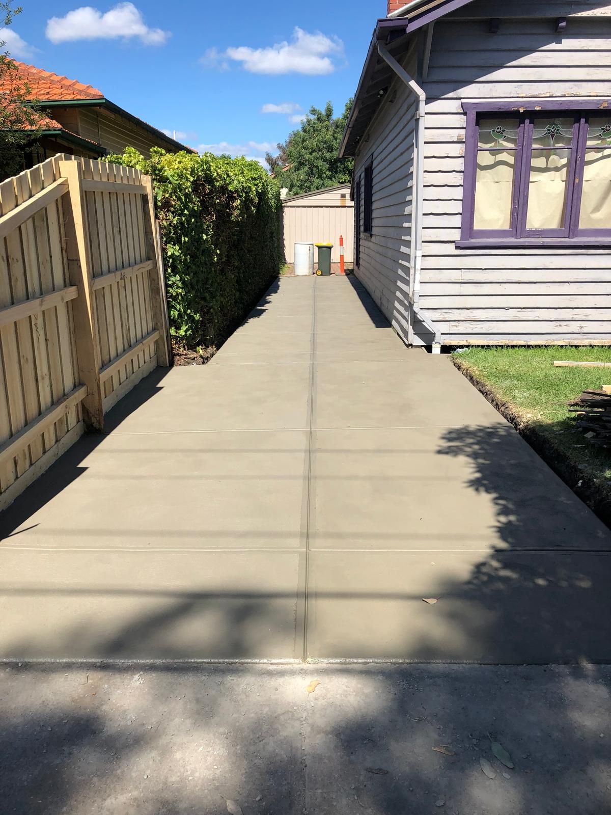 A concrete driveway leading to a house with a wooden fence.