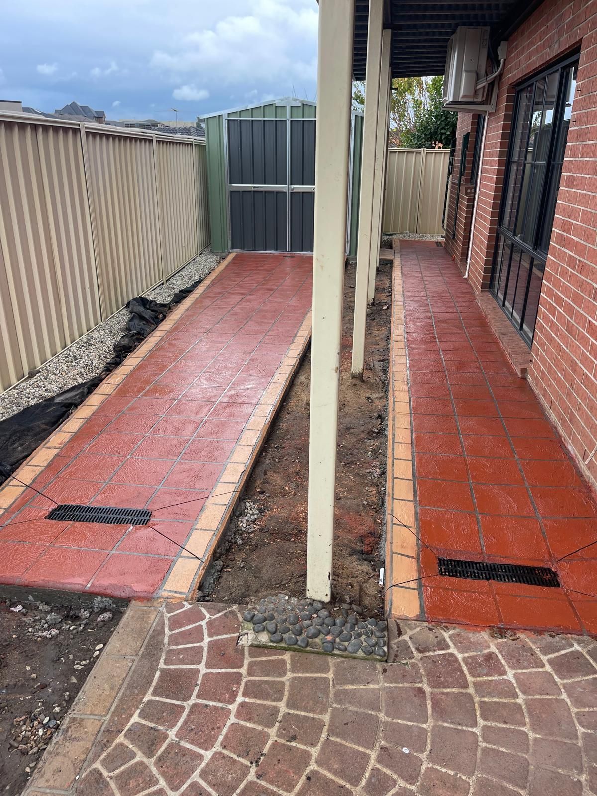 A brick walkway leading to a house with a fence in the background.