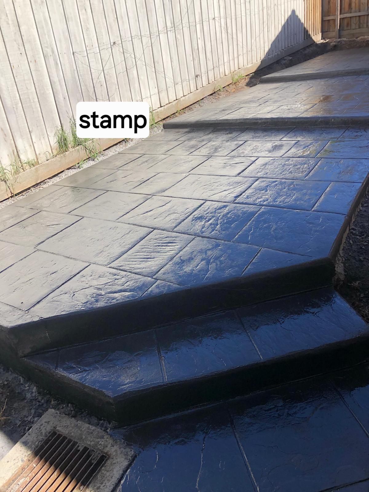 A stamped concrete walkway with steps and a fence in the background.