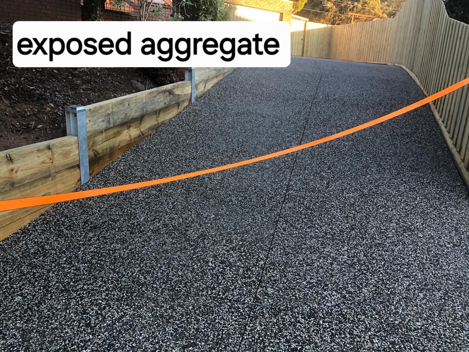 A gravel driveway with a wooden fence and a sign that says exposed aggregate.