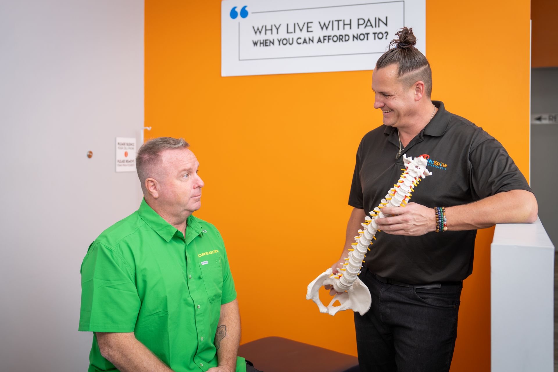 A man is holding a model of a spine while talking to another man.