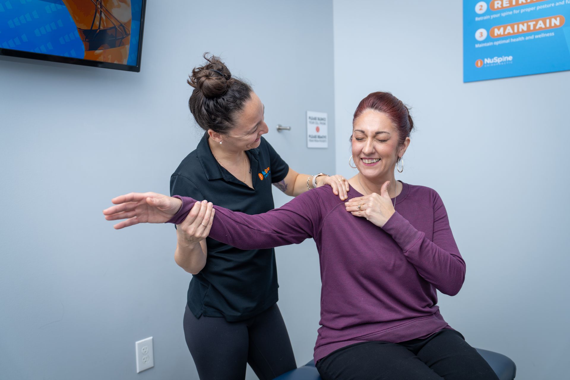 A woman is sitting on a table while a doctor examines her arm.