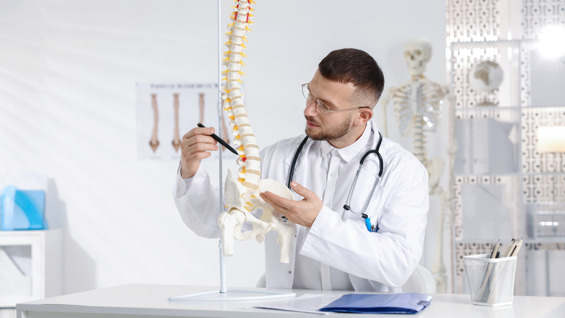 Doctor pointing at a spinal model in his office, explaining anatomy.