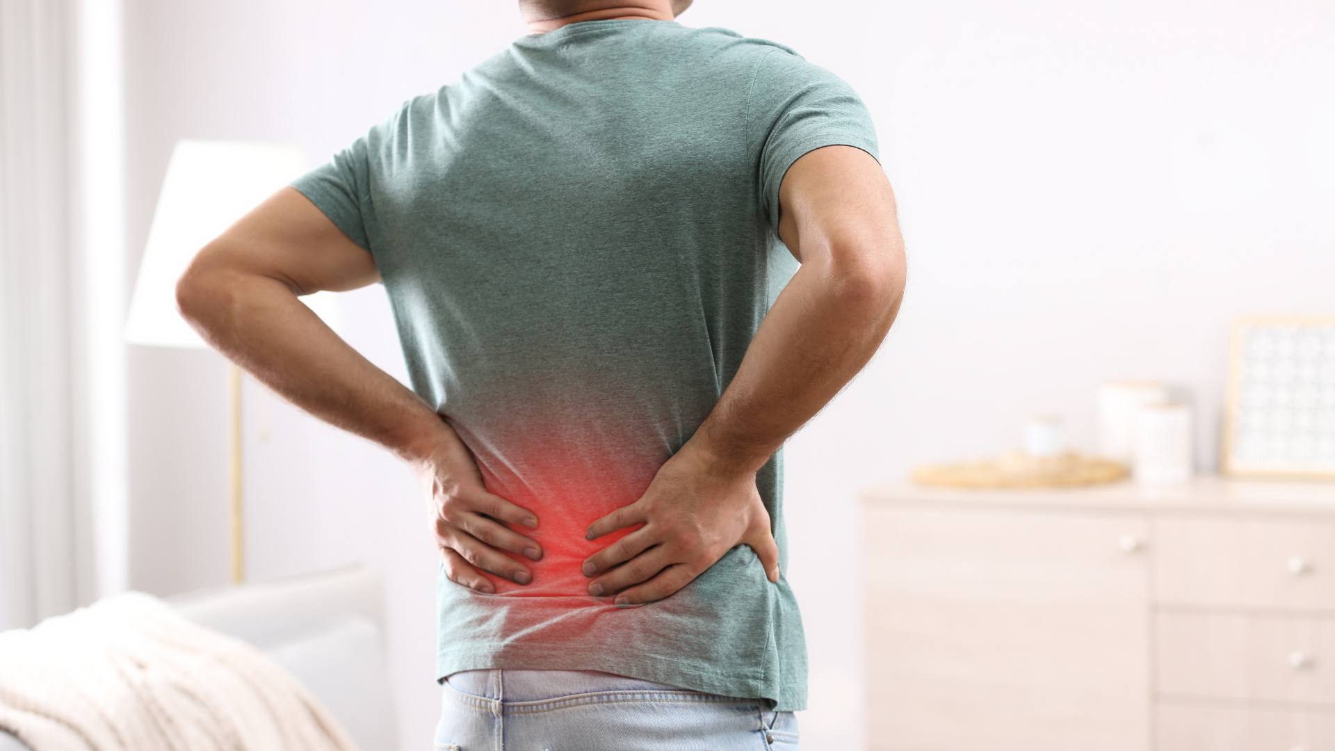 Man in green shirt holding his lower back, in pain. Red highlight indicates pain area.