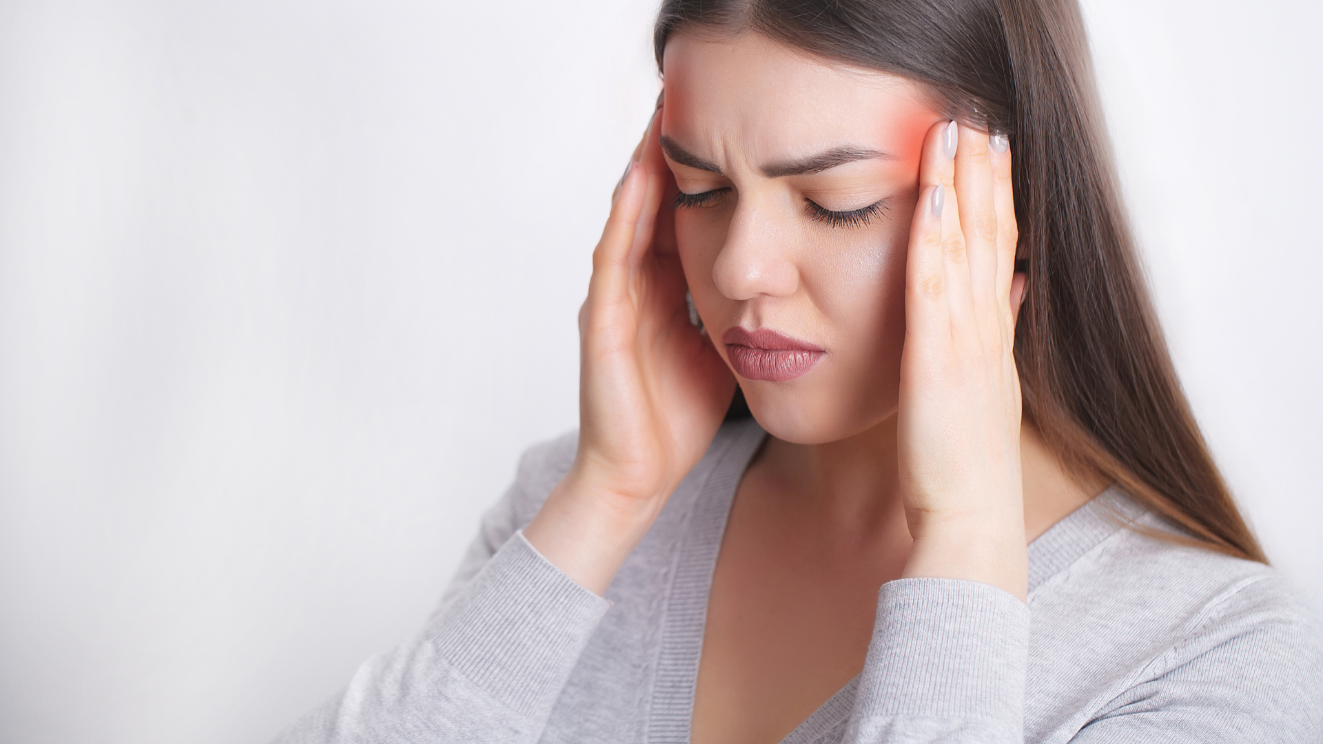 Woman with headache, holding temples, red mark on forehead, light grey shirt.