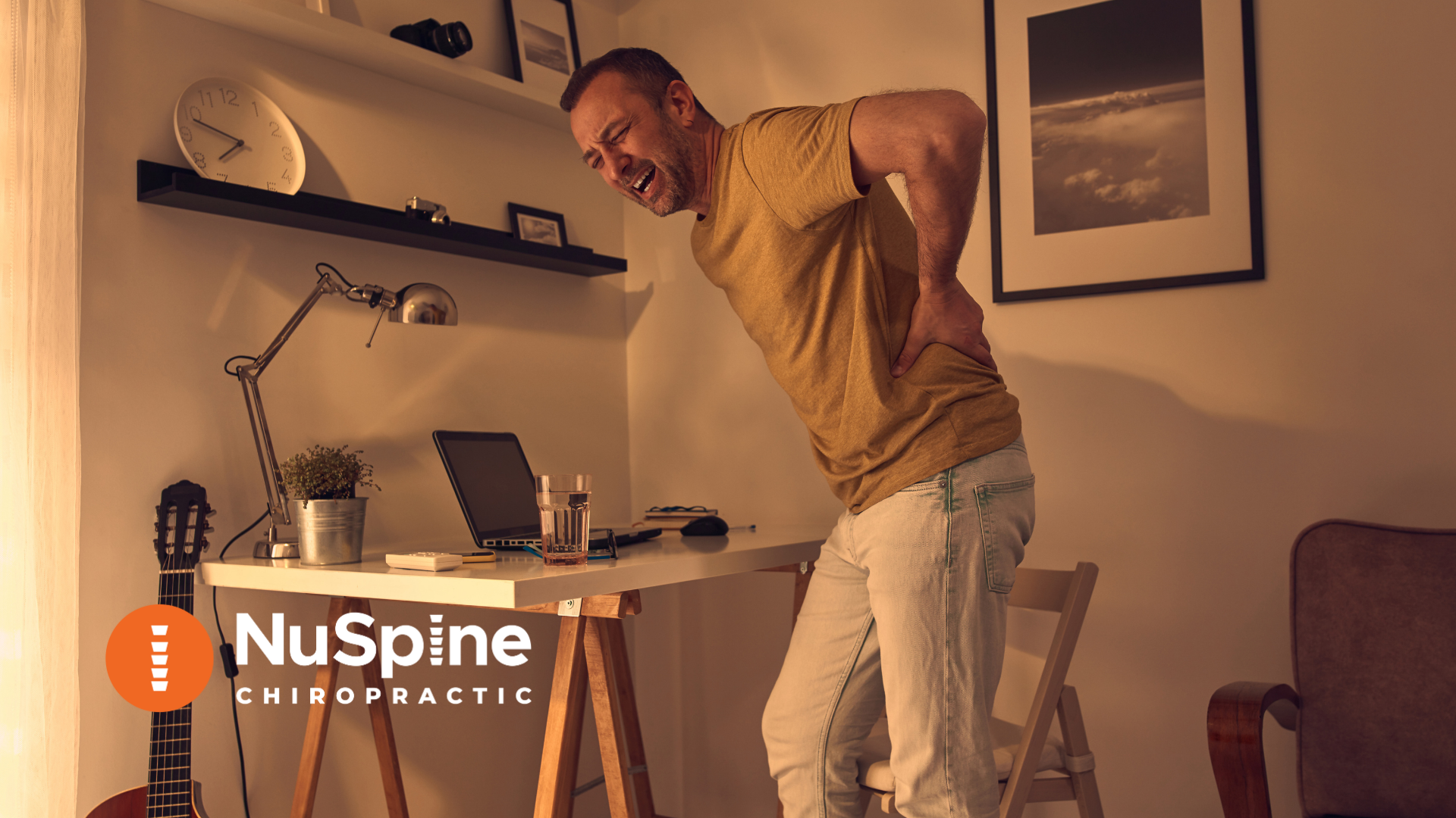 Man with back pain at a desk in his home office, holding his back in pain, NuSpine Chiropractic logo.
