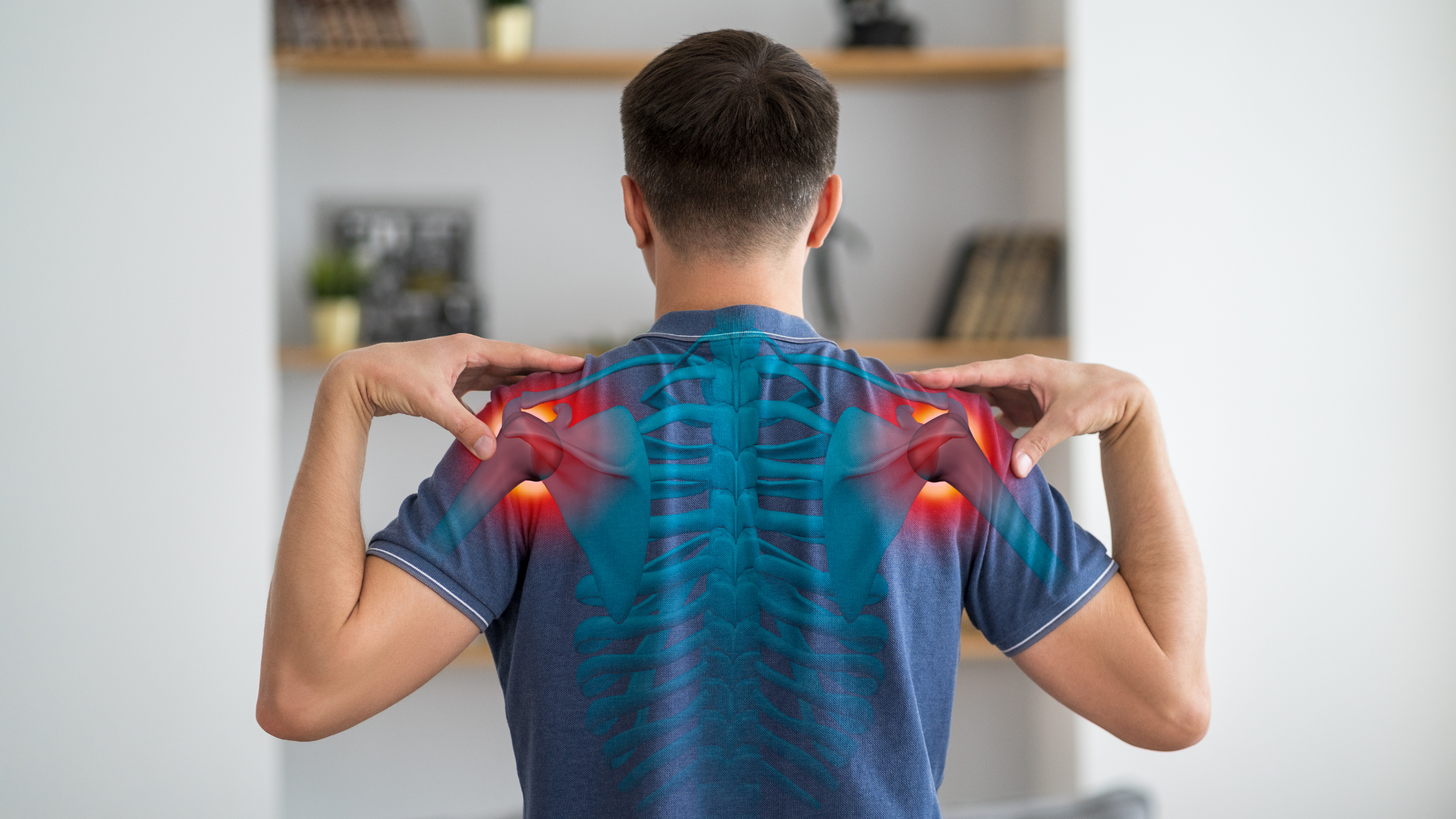 Man in a teal shirt holds his lower back in pain, indoors. Red glow highlights the pain area.