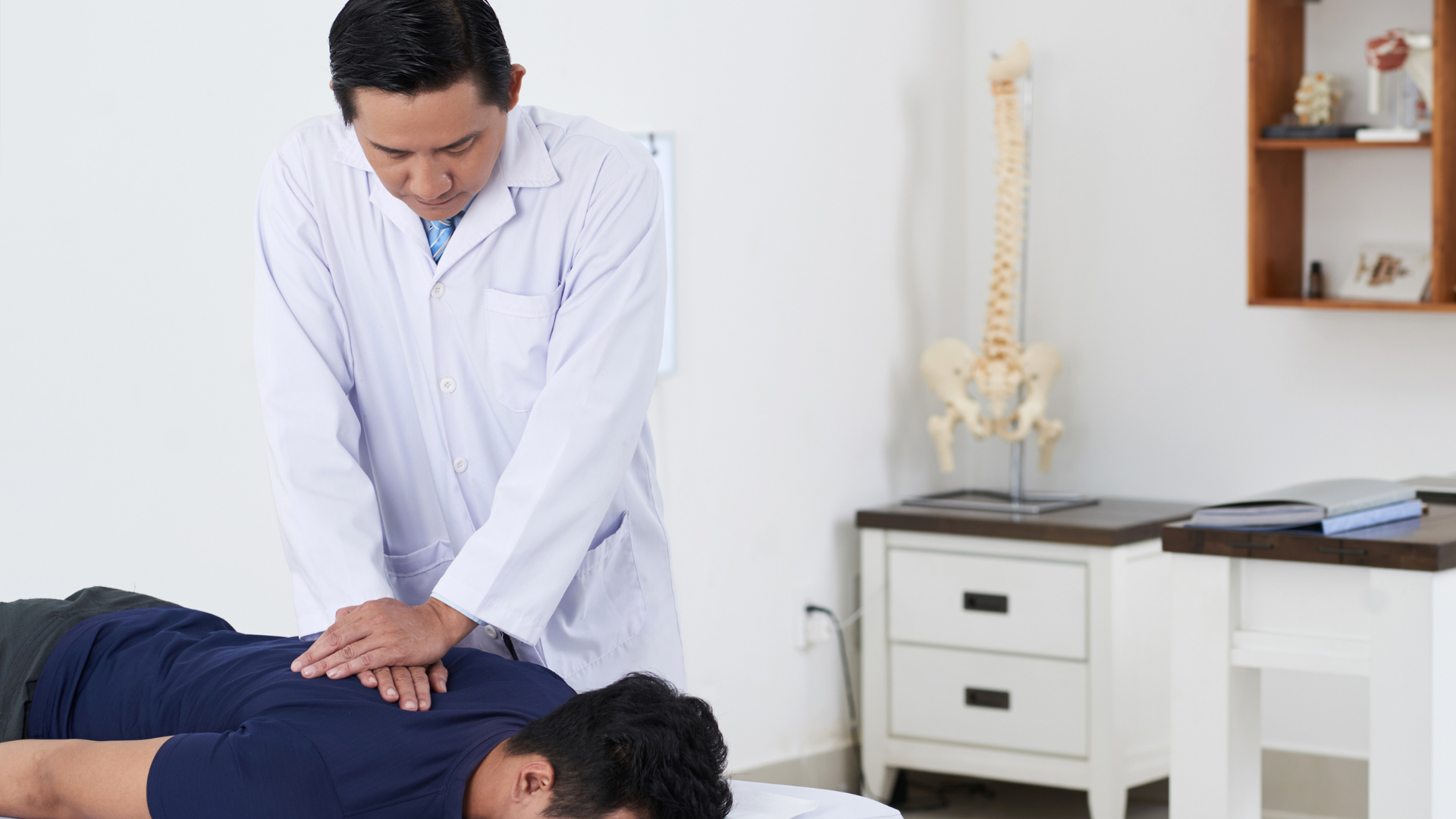 Chiropractor giving back adjustment to patient lying face down on table.