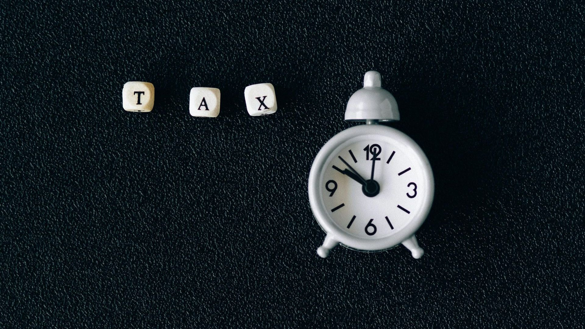 A white alarm clock is sitting next to a set of blocks that say tax.