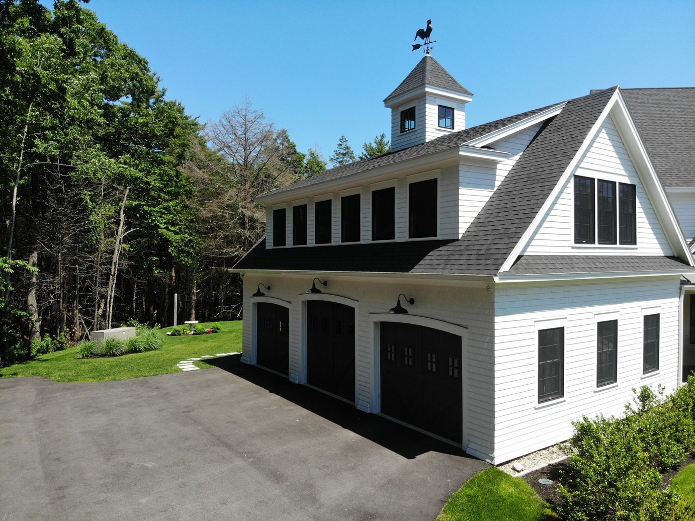 A white garage with black doors and a weather vane on top of it.