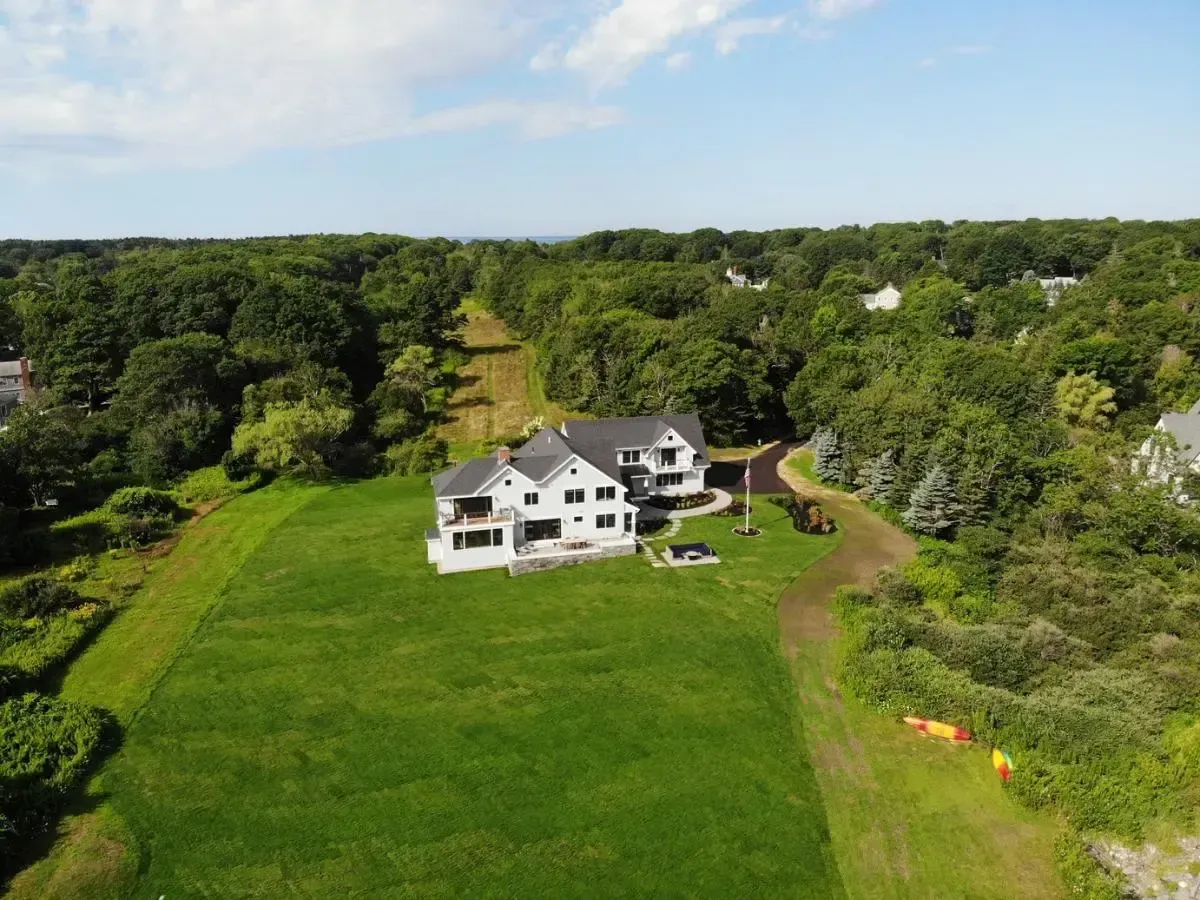 An aerial view of a large house in the middle of a lush green field surrounded by trees.