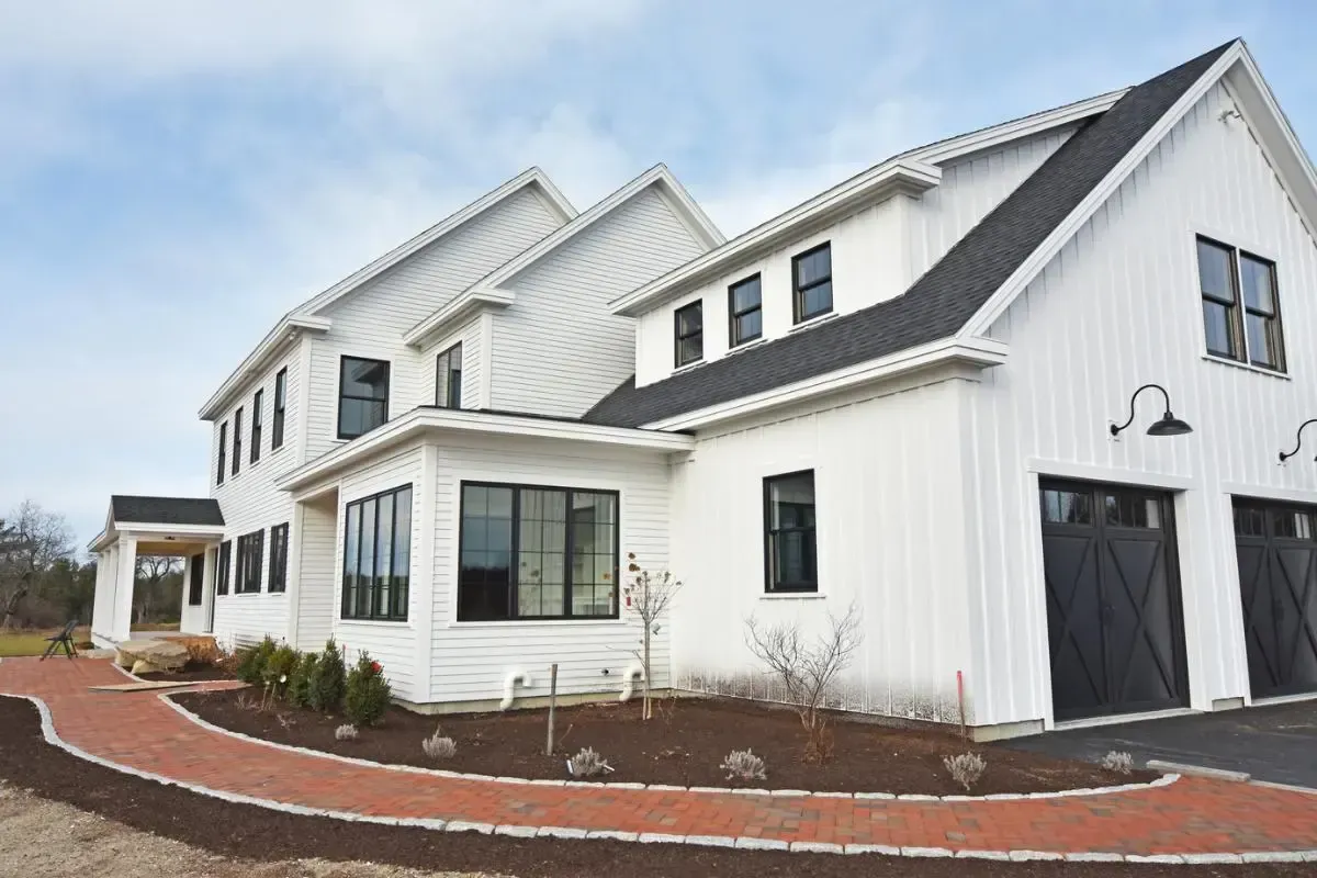 A large white house with a black roof and a brick walkway leading to it.