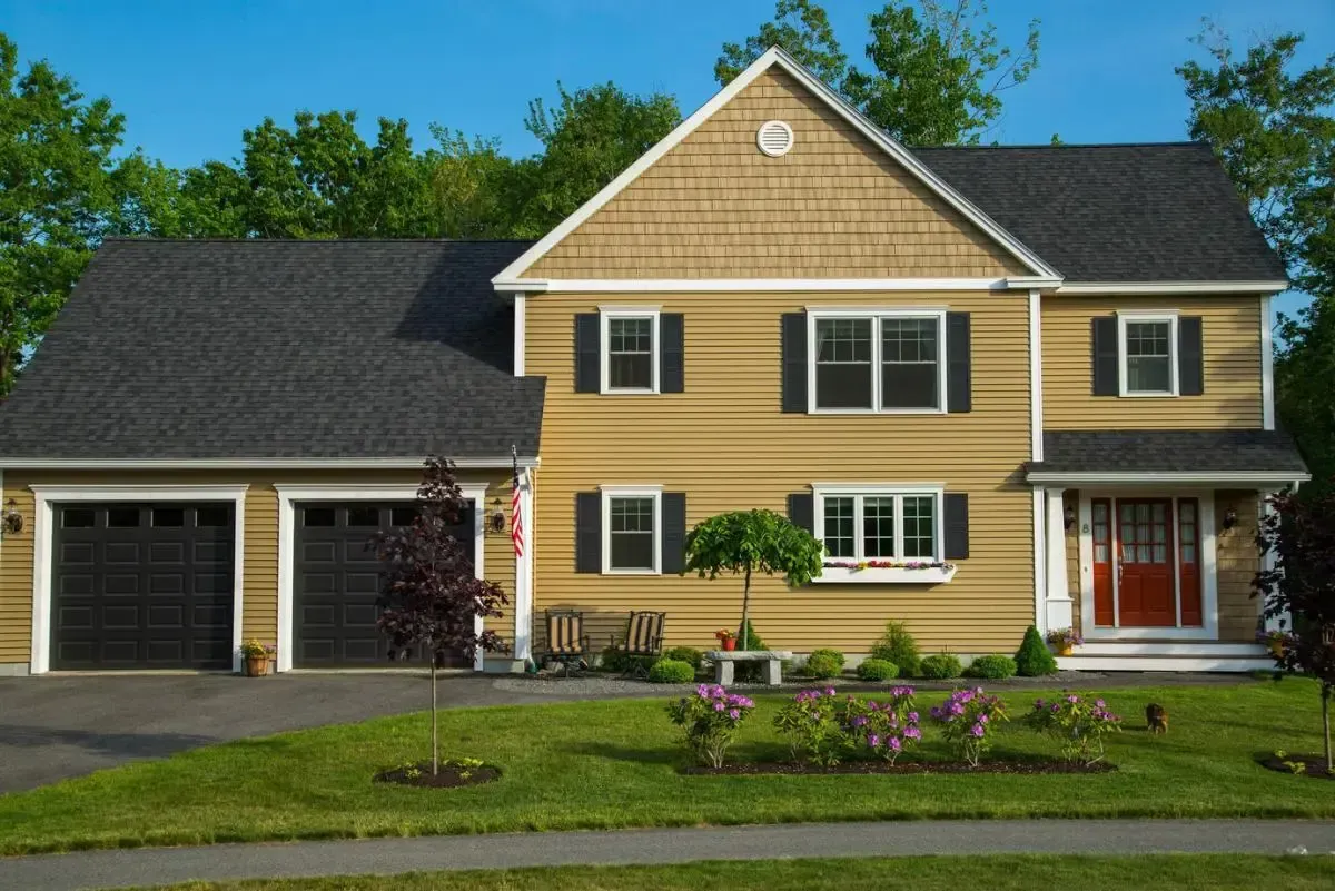 A large yellow house with a black roof and black garage doors