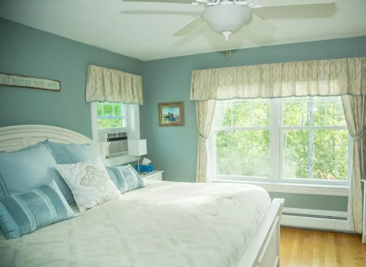 A bedroom with a bed , ceiling fan , window and blue walls.