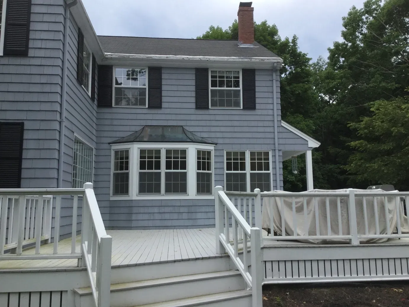A blue house with black shutters and a white deck