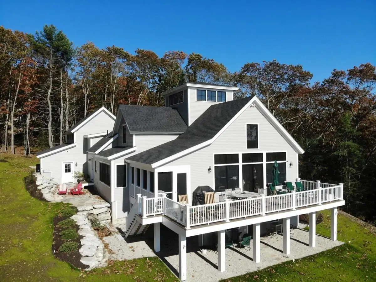 An aerial view of a large white house with a large deck surrounded by trees.