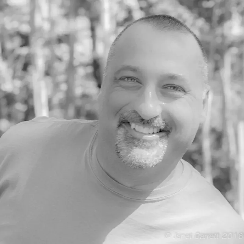 A man with a beard is smiling in a black and white photo.