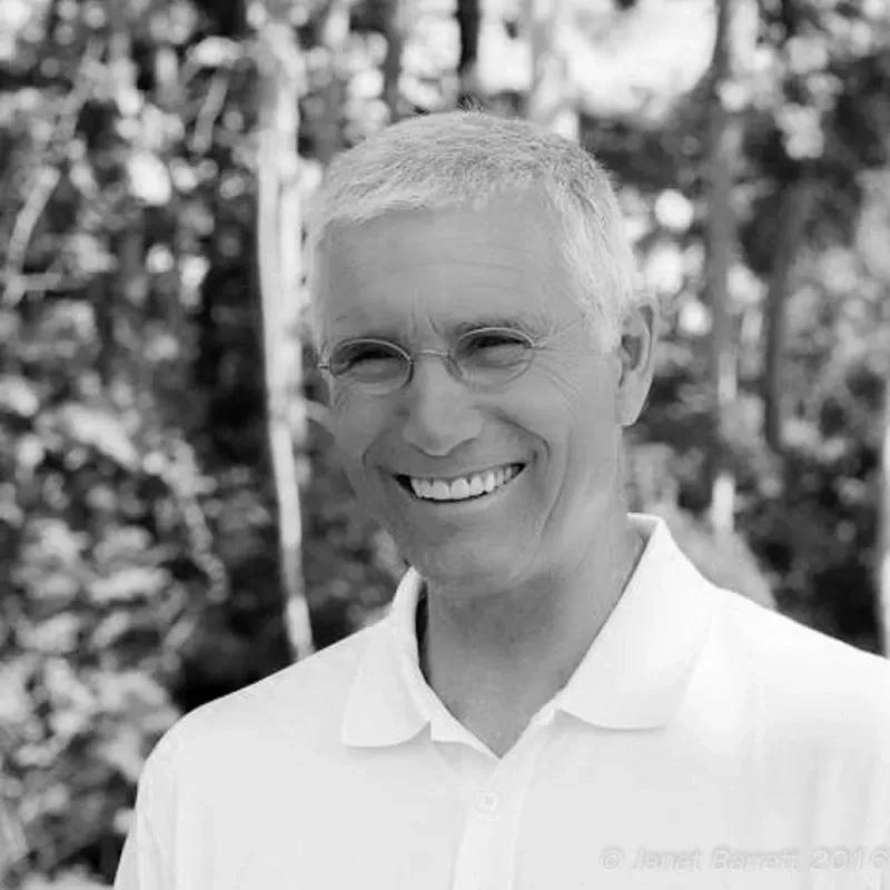 A man wearing glasses and a white shirt is smiling in a black and white photo.