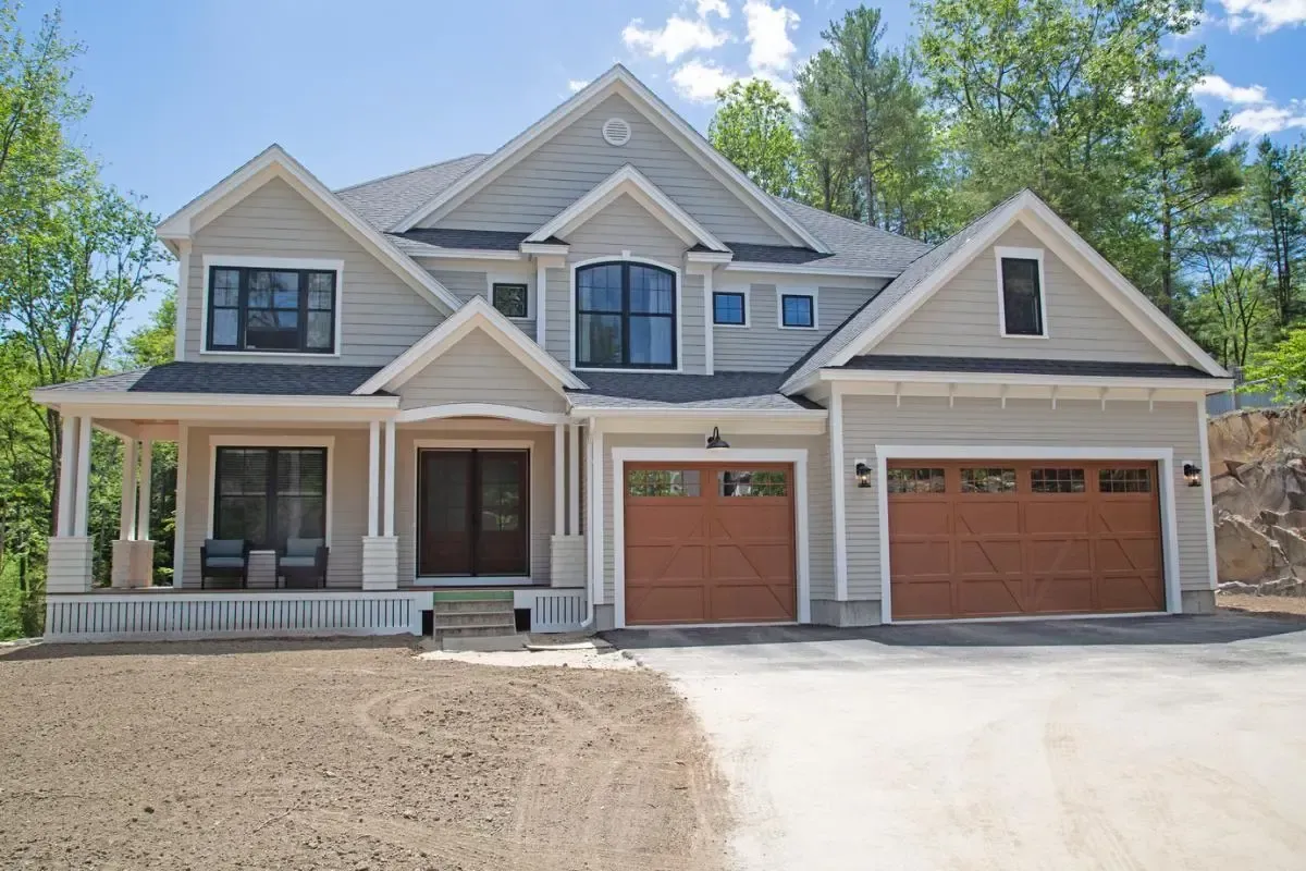 A two story house with 2 car garage and another door for one car with light brown garage doors.