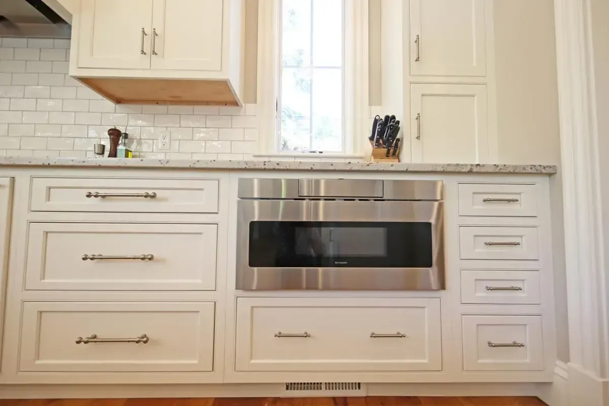 A kitchen with white cabinets and a stainless steel microwave oven.