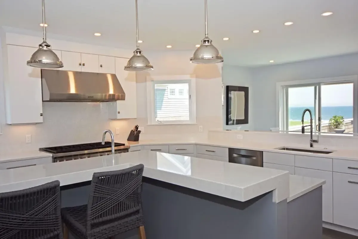 A kitchen with white cabinets , stainless steel appliances , and a large island with a view of the ocean.
