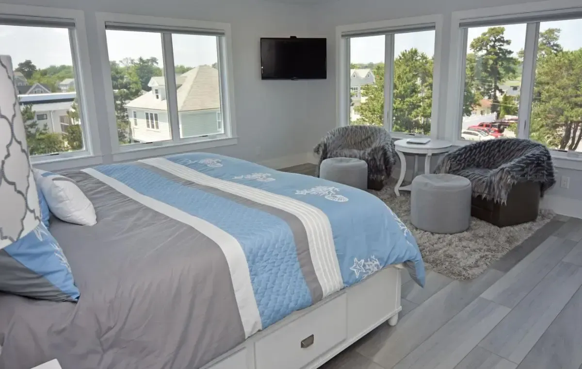 A bedroom with a king size bed , chairs , ottomans and a flat screen tv.
