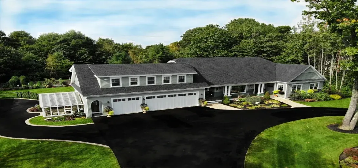 A large house with a black driveway is surrounded by trees and grass.