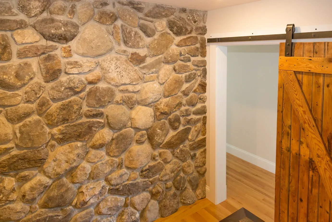 A stone wall with a sliding barn door in a room.