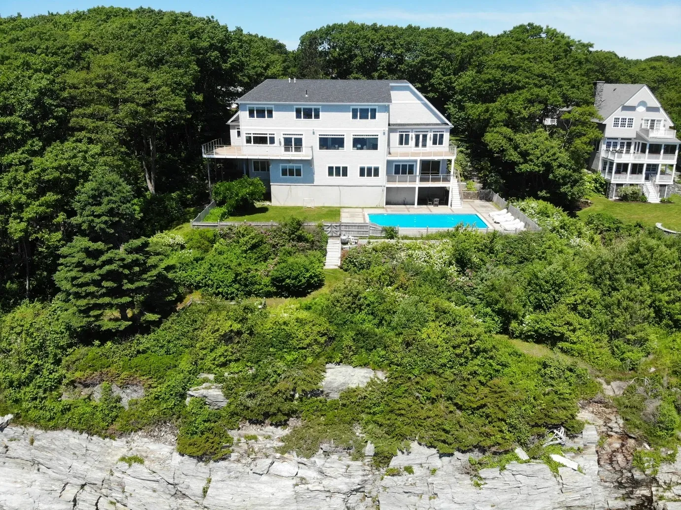 An aerial view of a large house with a pool on top of a hill surrounded by trees.