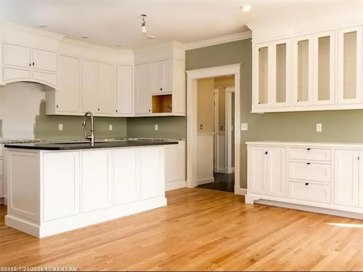 An empty kitchen with white cabinets and hardwood floors