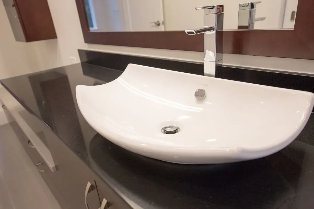 A bathroom sink with a black counter top and a mirror