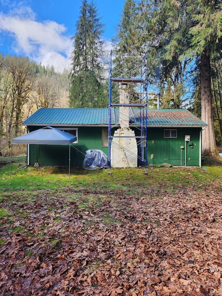 A green house with a chimney and a tent in front of it in the woods.