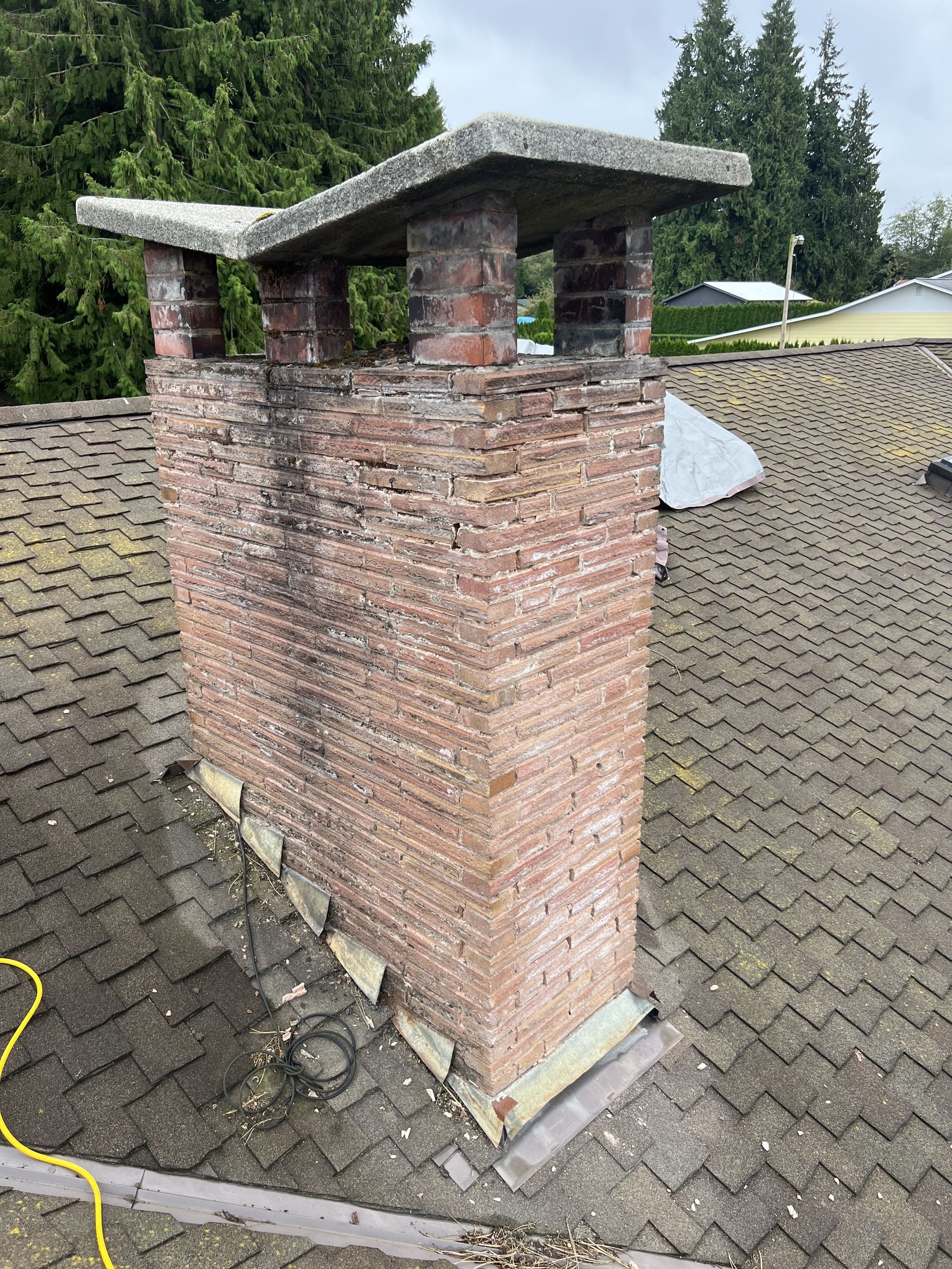 A brick chimney is sitting on top of a tiled roof.