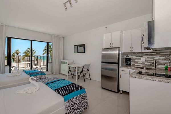 A hotel room with two beds , a kitchen , and a refrigerator.