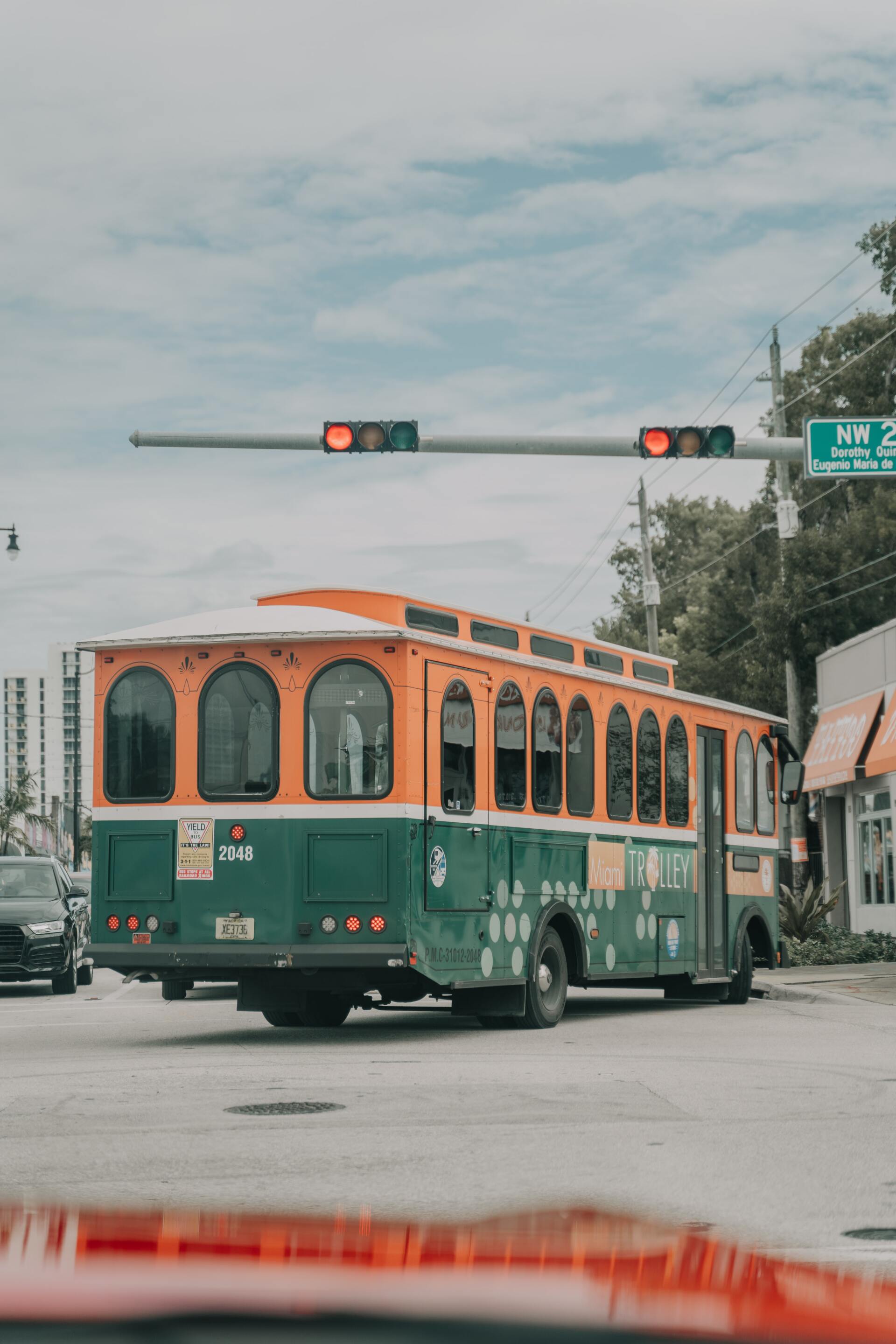 A green and orange bus is driving down a street.