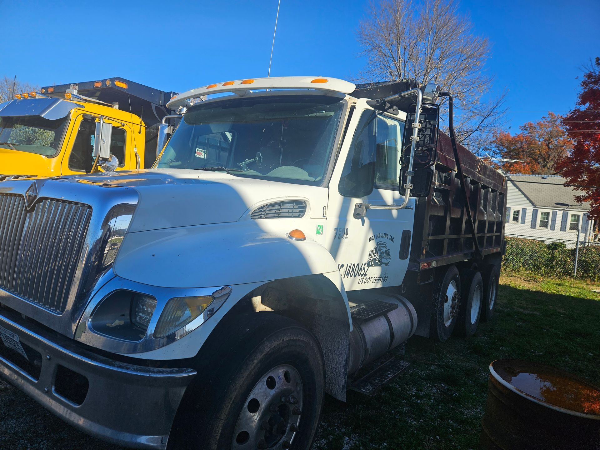 Three white semi-trucks parked on a highway, forest in the background.