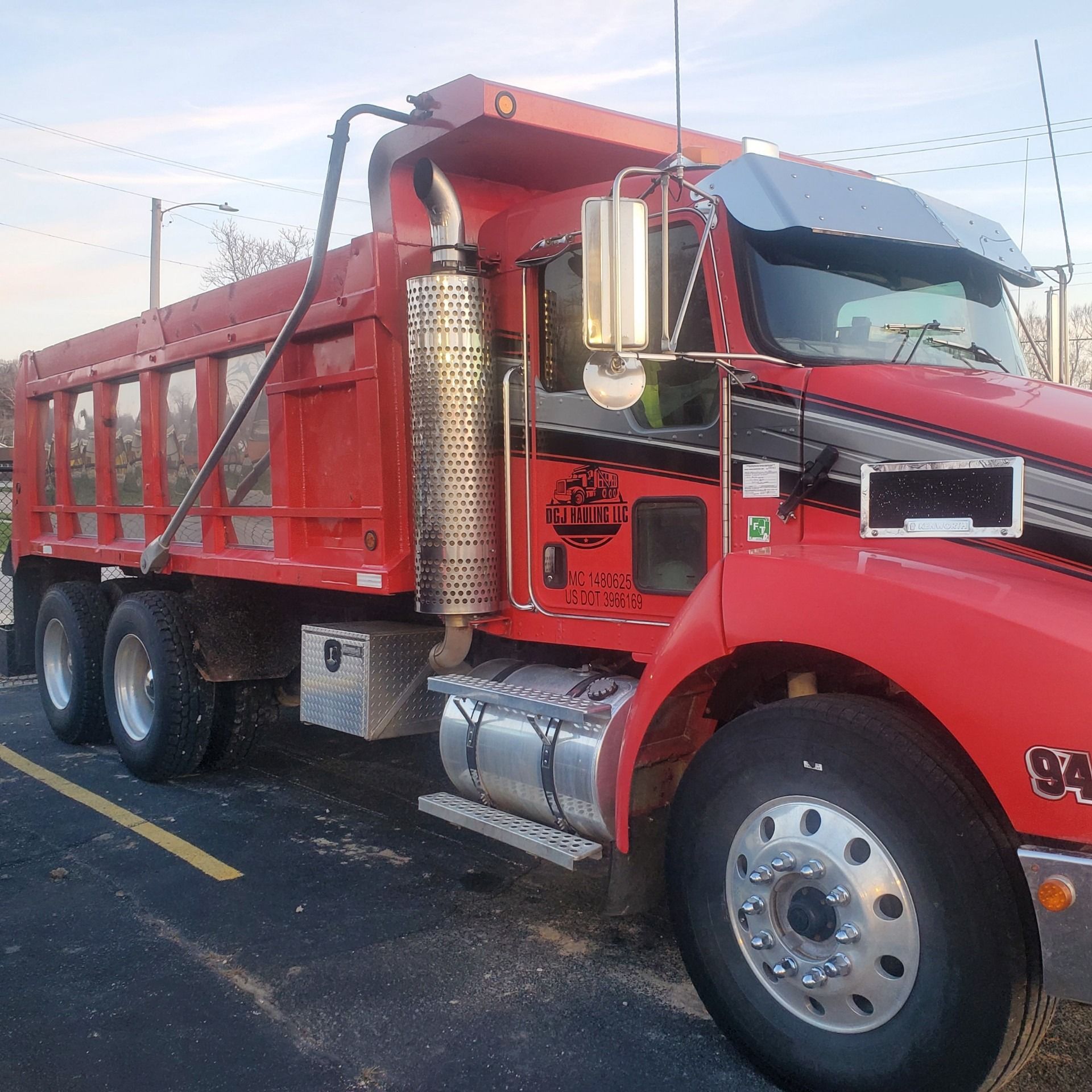 Red dump truck parked in a lot; the truck has a black stripe and silver exhaust stack.