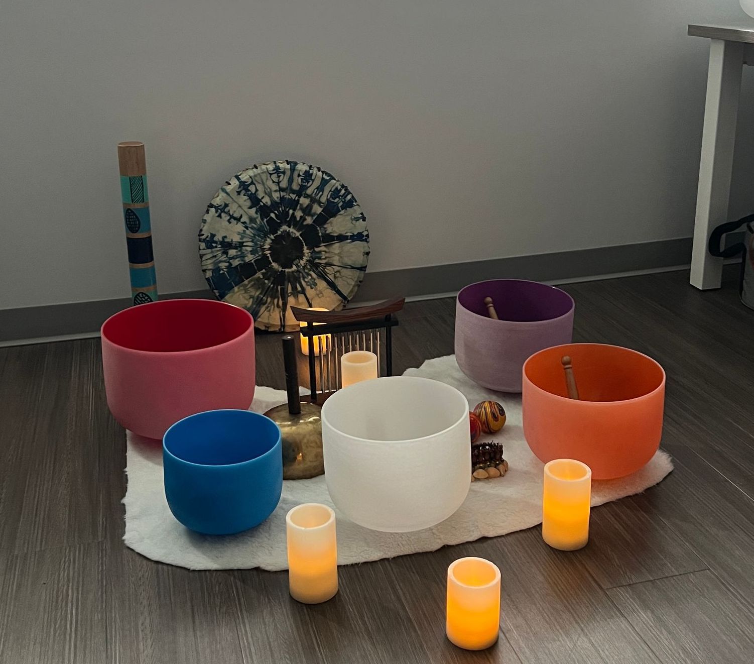 Several colored glass sound bowls sit on a rug on the floor with candles, prepping for a sound bath