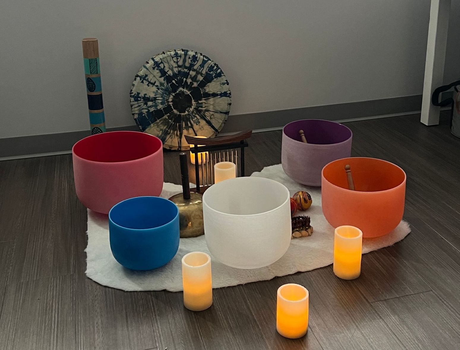 Several colored glass sound bowls sit on a rug on the floor with candles in preparation for a sound bath event